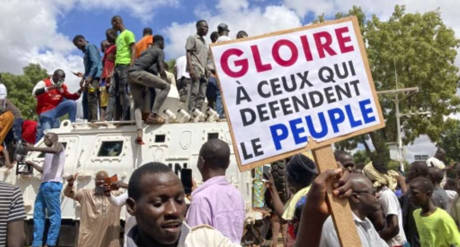 Protestors in the Burkina Faso Ouagadougou stand atop a UN armoured vehicle last weekend in support of the latest coup. The sign reads 'Glory to those who defend the people'.  By - AFP
