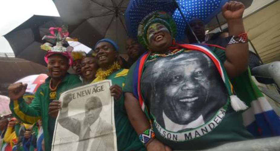 People hold portraits of Nelson Mandela during the memorial service of the South African former president at the FNB Stadium in Johannesburg on December 10, 2013.  By Alexander Joe AFP