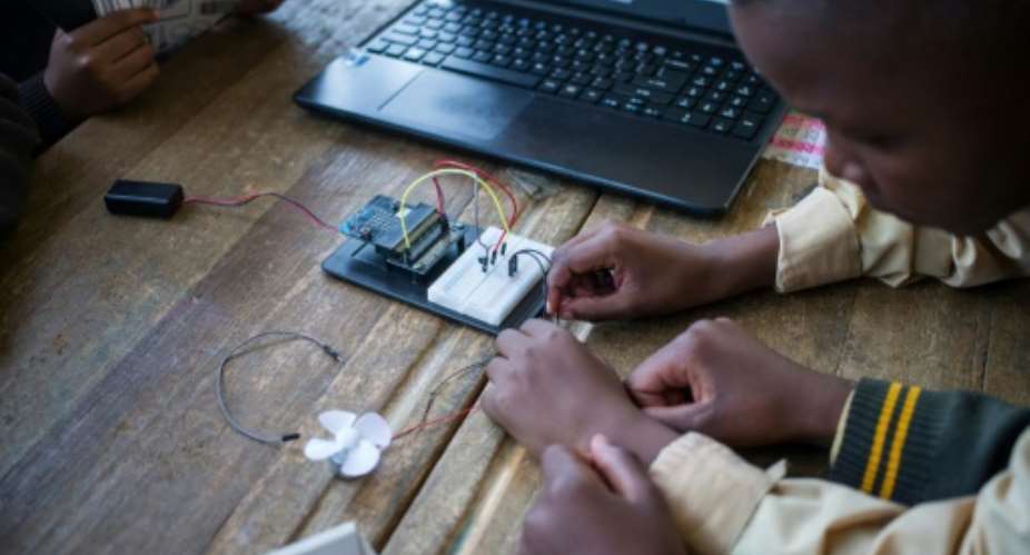Pupils at the coding club in Ivory Park take wires from the breadboard -- the base for building an electronics circuit -- to a fan that they will programmme to work from a laptop.  By WIKUS DE WET AFP