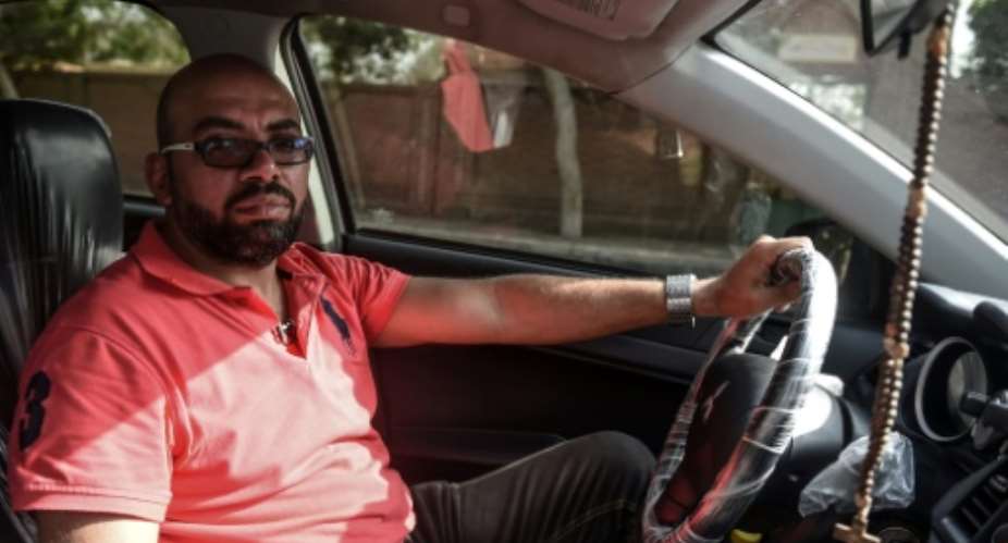 Ramez Wagih, an accountant in the morning and Uber driver in the afternoon, in his car in Cairo.  By MOHAMED EL-SHAHED AFP
