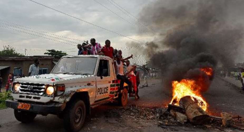 Protestors opposed to the Burundian president Pierre Nkurunziza's third term in office hitch a ride on a police vehicle past a burning barricade during a demonstration in the Cibitoke neighborhood of Bujumbura on May 19, 2015.  By Carl De Souza AFP