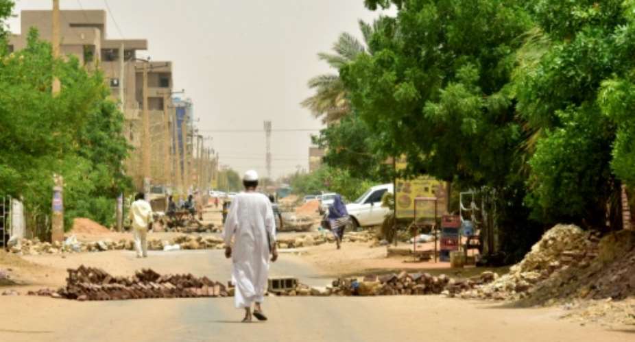 Residents walk past barricades in the Sudanese capital.  By - AFP