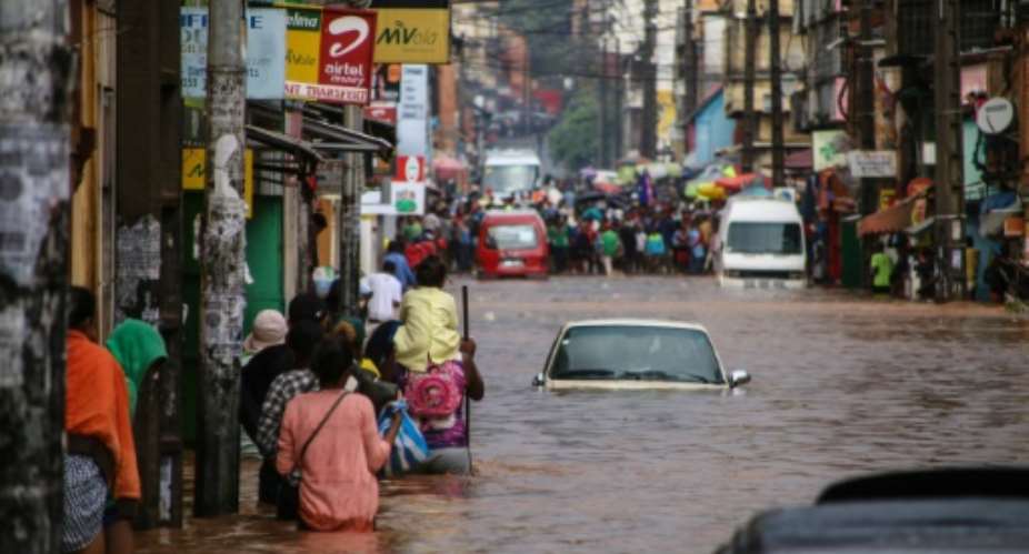 Residents walk through floodwaters past submerged vehicles on a road in the capital Antananarivo.  By MAMYRAEL AFPFile