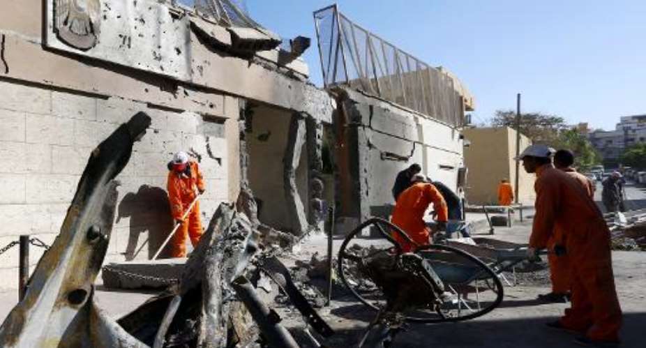 Municipality workers clean up the debris as Libyan security forces inspect the scene of a car bombing outside the United Arab Emirates embassy building in Tripoli on November 13, 2014.  By Mahmud Turkia AFPFile