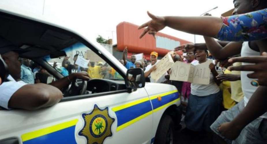 Protesters shout as a police car drives outside the Benoni court on March 8, 2013.  By Alexander Joe AFP
