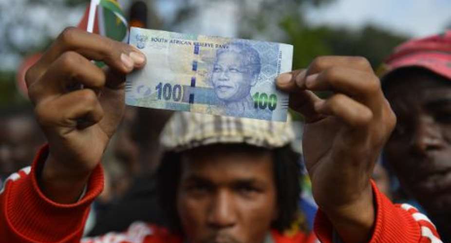 A man holds a 100 rand bill bearing the portrait of South African former president Nelson MandelaMandela as Mandela's funeral cortege drives through the streets in Pretoria on December 11, 2013.  By Odd Andersen AFPFile