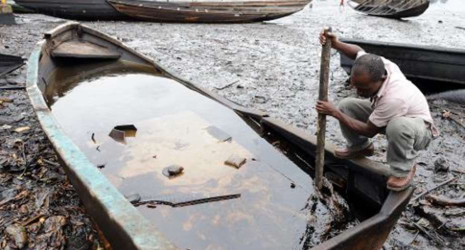 An indigene of Bodo, Ogoniland region in Rivers State, tries to separate with a stick the crude oil from water in a boat at the Bodo waterways polluted by oil spills attributed to Shell equipment failure August 11, 2011.  By Pius Utomi Ekpei AFPFile