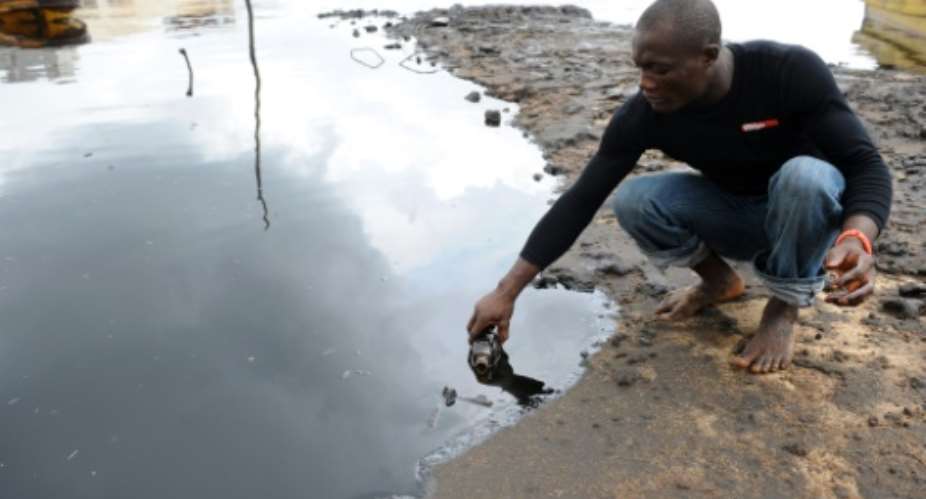 A man scoops spilled crude oil into a bottle from the waters of the Niger Delta swamps of Bodo, a village in Ogoniland, on June 24, 2010.  By Pius Utomi Ekpei AFPFile