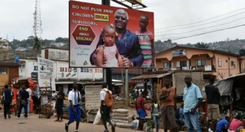 People walk under an Ebola's information board featuring Sierra Leone's president Ernest Bai Koroma on January 22, 2016 in a street of Freetown..  By Sia-Kambou AFPFile