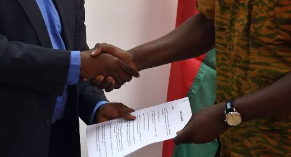 Henry Ye, president of the commission representing the main power players, hands the transition charter to Burkina Faso's army-appointed leader, Lieutenant-Colonel Isaac Zida during a meeting in Ouagadougou on November 14, 2014.  By Issouf Sanogo AFP