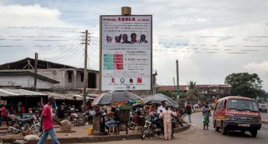 People walk in front of a poster warning against the deadly Ebola virus in a street of Freetown on October 4, 2014.  By Florian Plaucheur AFPFile