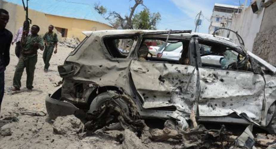 Somali government soldiers walk around a destroyed car at the site of car bomb blast in front of the Makka Al Mukarrama Hotel in Mogadishu, on March 15, 2014.  By Mohamed Abdiwahab AFPFile