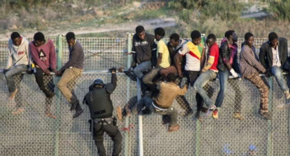 A member of the Spanish Guardia Civil climbs the border fence as would-be immigrants sit on top, in Melilla on October 22, 2014.  By Blasco Avellaneda AFPFile