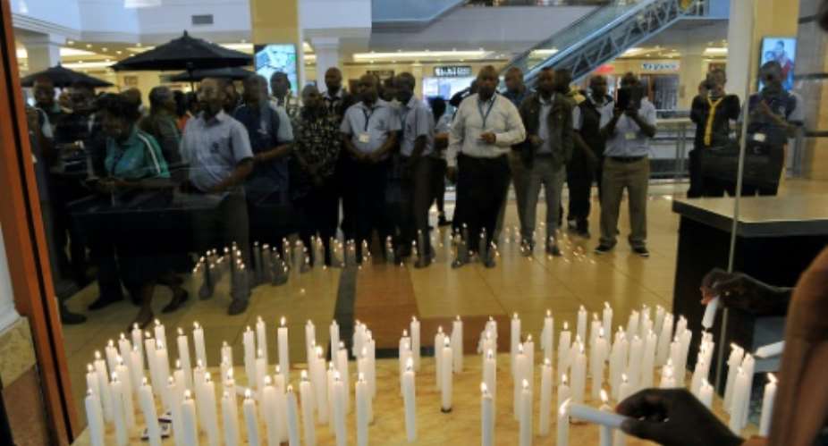 Staff of the Nakumatt supermarket chain gather in front of candles lit to mark the second anniversary commemorations of the Westgate shopping mall attack by militants.  By SIMON MAINA AFPFile