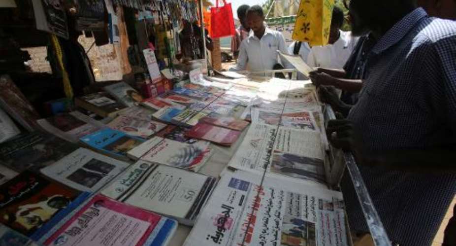 Sudanese men look at newspapers displayed at a kiosk in the capital Khartoum on February 16, 2015.  By Ashraf Shazly AFP