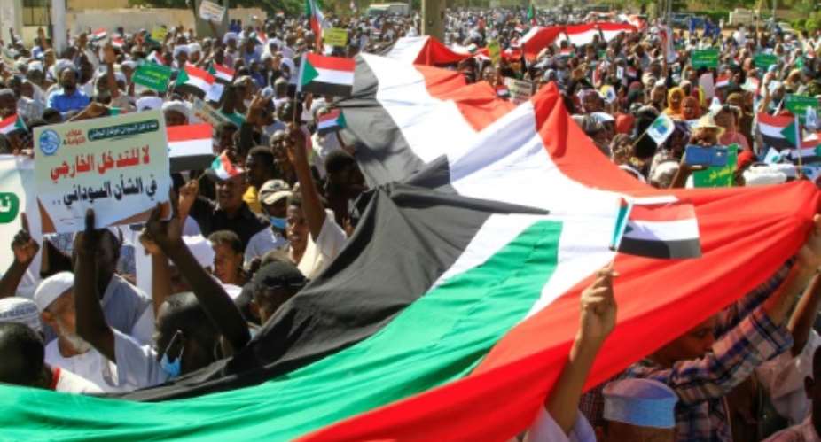 Sudanese protesters carry a giant national flag outside the UN headquarters in Khartoum on Saturday.  By Ebrahim Hamid AFP
