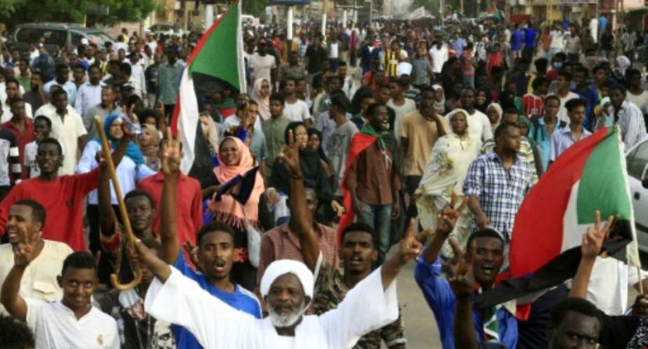 Sudanese protesters chant slogans and flash the victory sign as they march with national flags during a mass demonstration against the country's ruling generals in Khartoum.  By Ebrahim Hamid AFP
