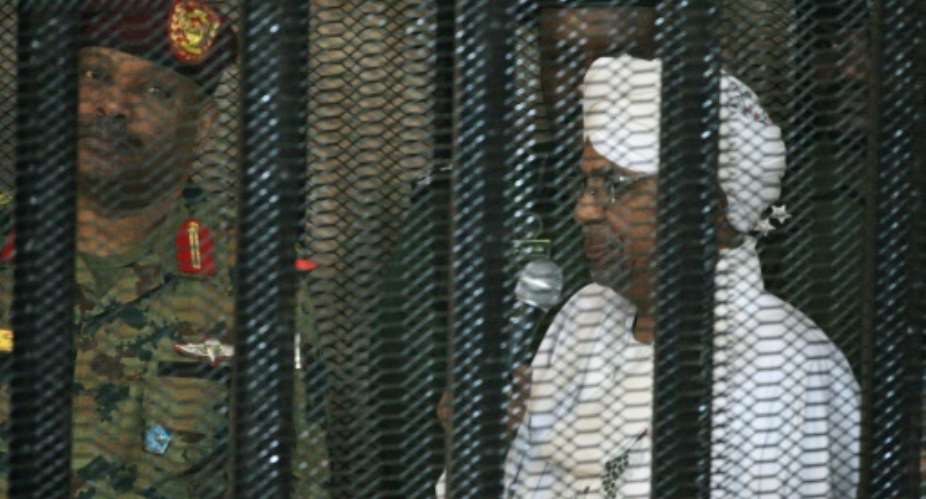 Sudan's deposed military ruler Omar al-Bashir stands in a defendant's cage at the opening of his corruption trial in Khartoum in August.  By Ebrahim HAMID AFP