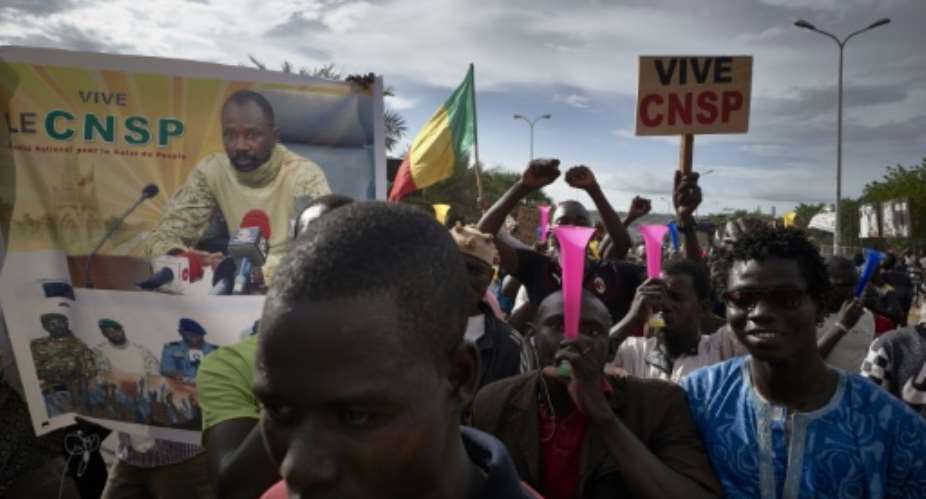 Supporters of the junta, which calls itself the CNSP National Committee for the Salvation of the People, walk past a banner depicting its leader Assimi Goita in a rally in Bamako on Wednesday.  By MICHELE CATTANI AFP