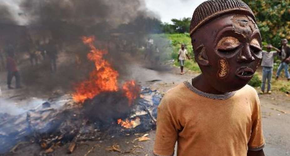 A protestor opposed to Burundian President Pierre Nkurunziza seeking a third consecutive term in office, wears a mask near a burning barricade in the Kinama  neighborhood of Bujumbura on May 25, 2015.  By Carl de Souza AFPFile
