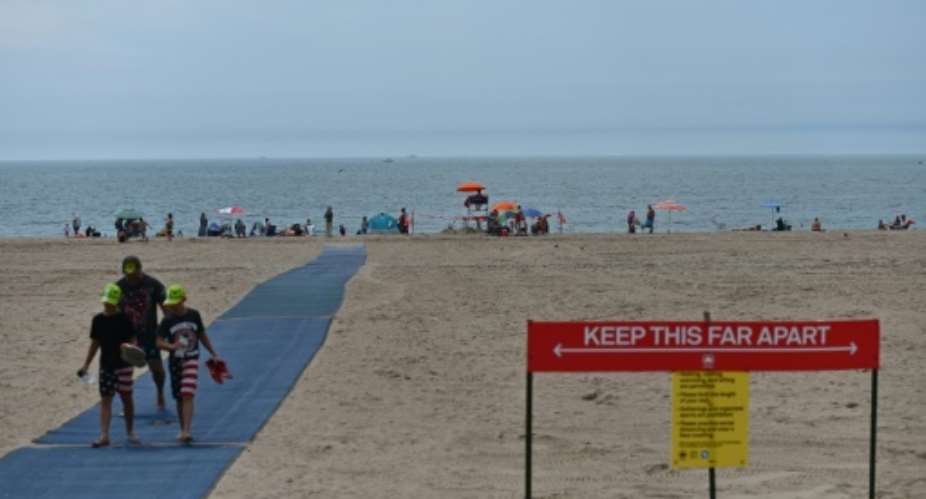 The Coney Island beach in New York City may be open, but the sign makes it clear how far away you should stay from people to remain safe from COVID-19.  By Angela Weiss AFP