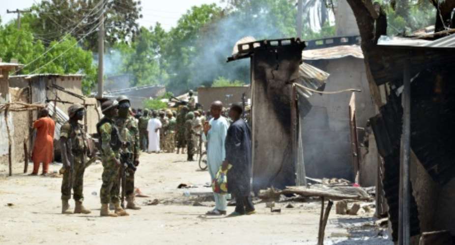 Soldiers speak to people standing near houses burnt by Boko Haram Islamists in Zabarmari, a fishing and farming village near Maiduguri, on July 3, 2015.  By  AFPFile