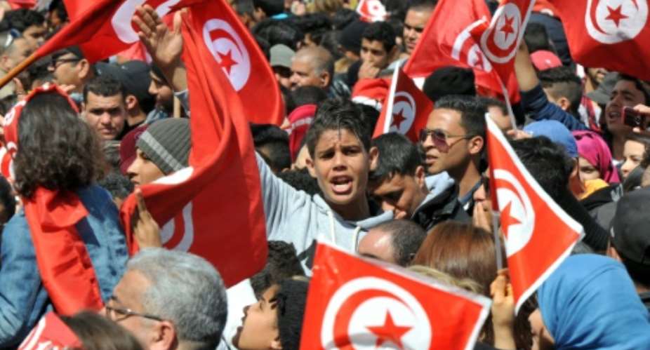 A photo taken on March 29, 2015 shows Tunisians waving their national flag and chanting slogans during a march against extremism outside Tunis' Bardo Museum.  By Fethi Belaid AFPFile