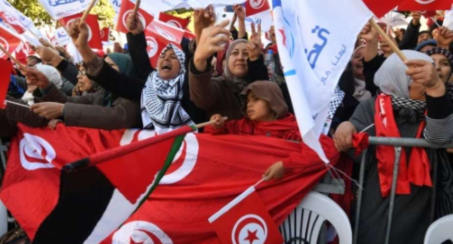 Tunisians wave their national flag and the flag of the Ennahda Islamist party as they gather on Habib Bourguiba Avenue in Tunis on January 14, 2018 to mark the seventh anniversary of the uprising that launched the Arab Spring.  By FETHI BELAID AFP