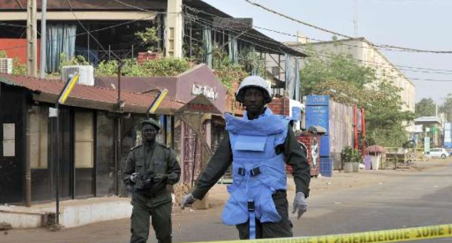 Policemen stand near the La Terrasse restaurant -- seen in the backround with the blue curtains -- in Bamako on March 7, 2015, after five people were shot dead overnight in a suspected terror attack.  By Habibou Kouyate AFP