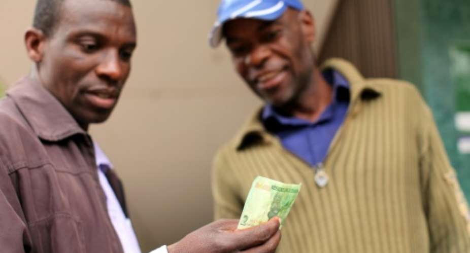 Two men look at a bond note released by the Reserve Bank Of Zimbabwe in the capital Harare.  By Wilfred Kajese AFP