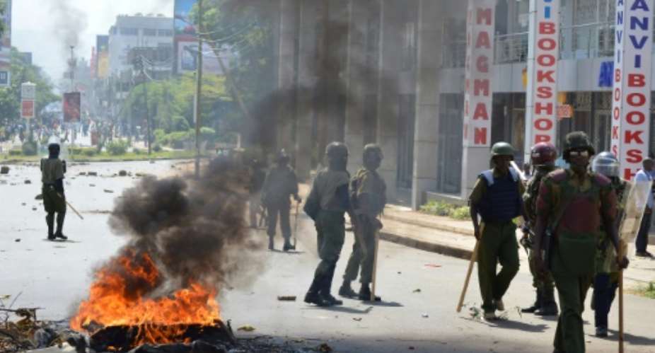 Police officers walk past burning tyres in Kisumu, Kenya, on June 6, 2016.  By  AFP