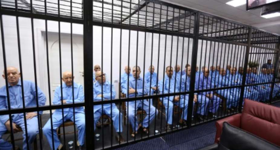 Former aides of Libyan dictator Moamer Kadhafi sit dressed in prison blue behind the bars of the accused cell during their trial on July 28, 2015 in Tripoli.  By Mahmud Turkia AFP