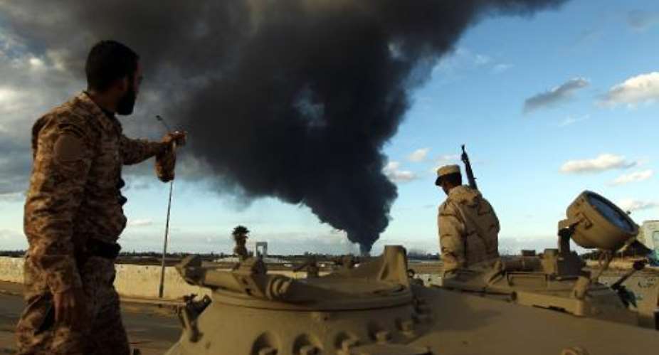 Members of the Libyan army stand on a tank as heavy black smoke rises from the port in Benghazi on December 23, 2014.  By Abdullah Doma AFP