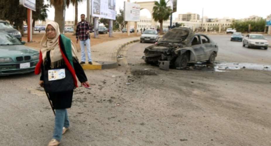 A woman walks near a damaged car after shelling hit a demonstration in Benghazi calling for military forces to re-capture the city of Sirte from Islamic State group without foreign intervention on May 6, 2016.  By Abdullah Doma AFPFile