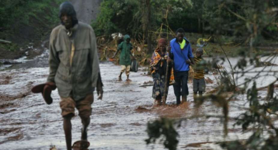 Villagers cross through receding waters in an area of flash flooding at Solai in Kenya's  Nakuru County after a private dam used for irrigation and fish farming burst its banks leaving at least 44 people dead..  By TONY KARUMBA AFP