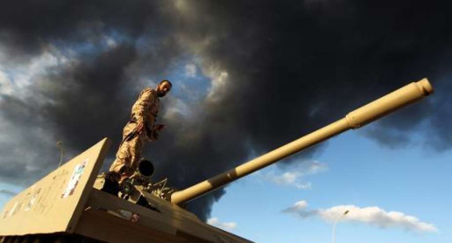 A member of the Libyan army stands on a tank as heavy black smoke rises from Benghazi port on December 23, 2014.  By Abdullah Doma AFPFile