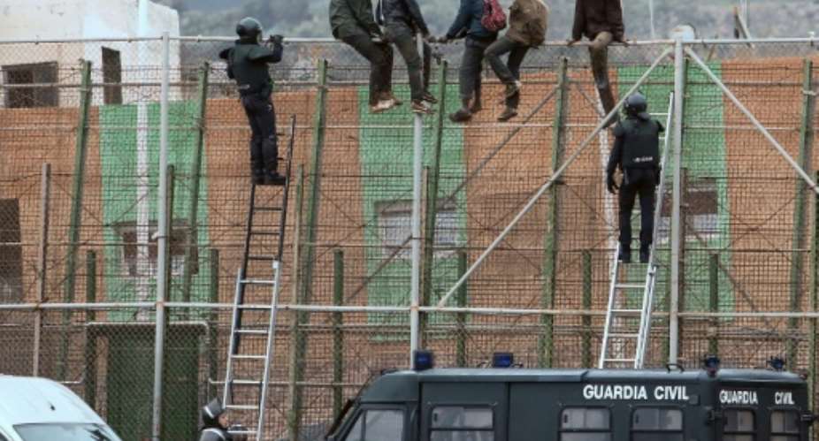 Watched by Spanish police in 2015, would-be immigrants sit atop a border fence separating Morocco from the north African Spanish enclave of Melilla, where some 200 people vaulted over the barrier Saturday.  By ANGELA RIOS AFPFile