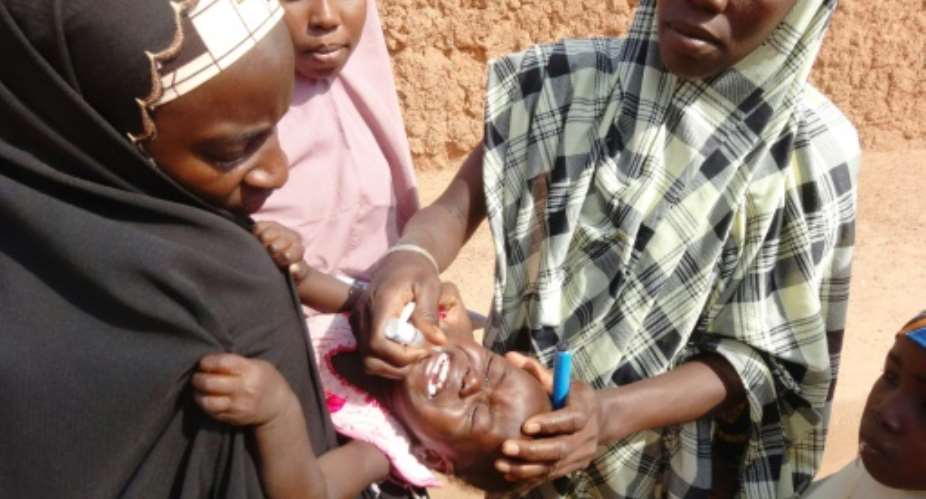 A woman administers an oral polio vaccine to a child in the Dawanau district of Kano, northern Nigera, during an immunization campaign, October 28, 2013.  By Aminu Abubakar AFPFile