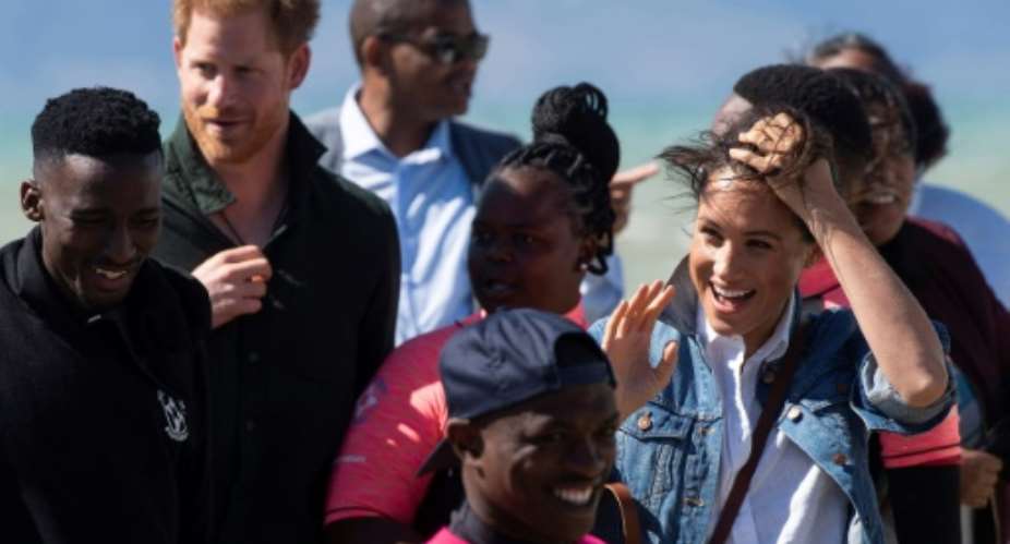 Wind and smiles: Prince Harry and his wife Meghan meet members of Waves for Change. The group uses surfing to help young people trapped in Cape Town's slums get a different perspective on life.  By DAVID HARRISON AFP