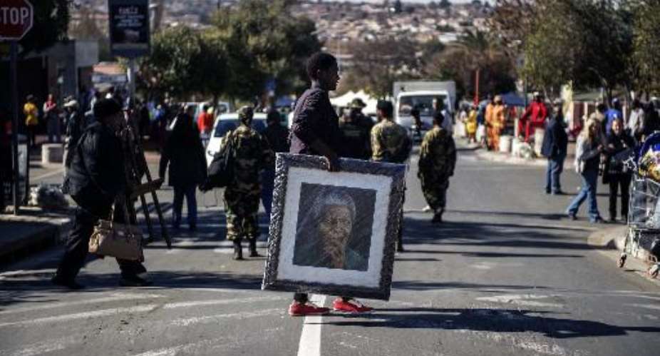 A woman carries a painting of late Nelson Mandela outisde his former house in Soweto on July 18, 2014.  By Gianluigi Guercia AFP