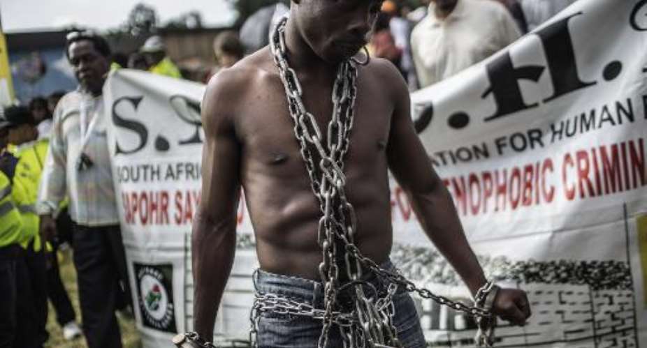 An anti-xenophobia activist stands chained in front of a banner, as thousands of people get ready to march against the recent wave of xenophobic attacks in South Africa through the streets of Johannesburg CBD on April 23, 2015.  By Gianluigi Guercia AFP