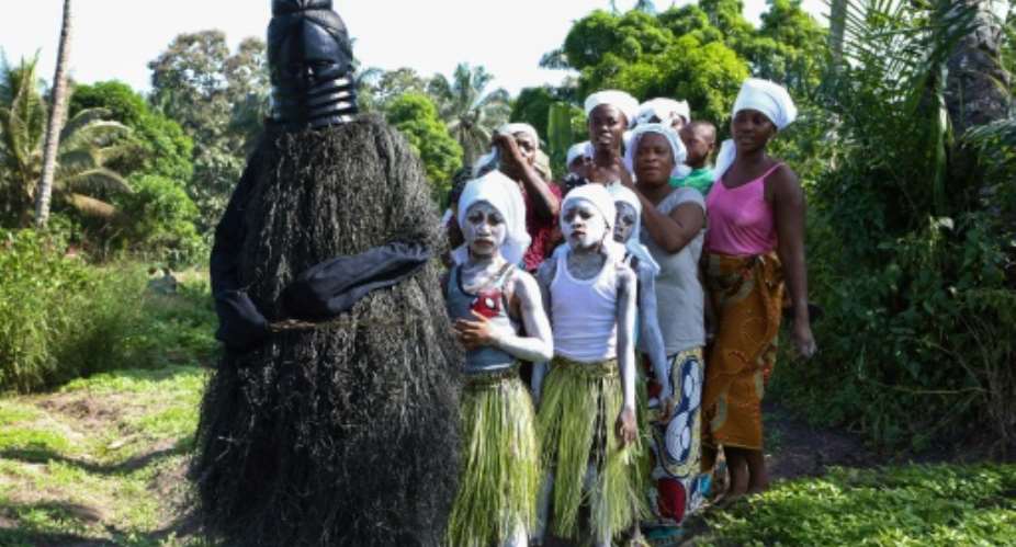 Young girls in white face paint take part in a procession to start their initiation into the Bondo secret society, alongside a figure called the Black Devil.  By LYNN ROSSI AFP