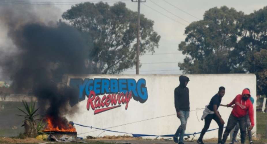 Young men haul a burning tyre during protests at Tygerberg Raceway near Cape Town. The motor-racing venue was invaded on August 6 by people demanding land.  By RODGER BOSCH AFP