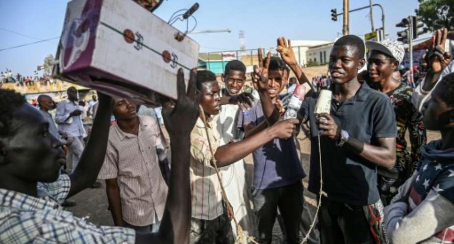 Young Sudanese protesters mimic journalists -- complete with a cardboard mocked up camera and a plastic bottle to represent a microphone -- to poke fun at state TV for failing to cover demonstrations.  By OZAN KOSE AFPFile