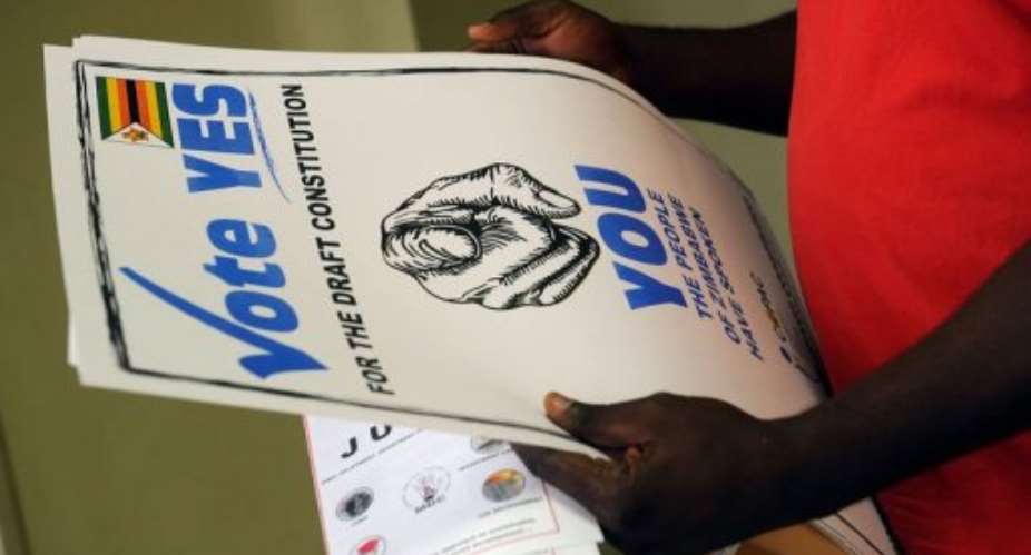 A man holds up posters calling on Zimbabweans to vote yes for the constitutional referendum in Harare on March 14, 2013.  By Alexander Joe AFP