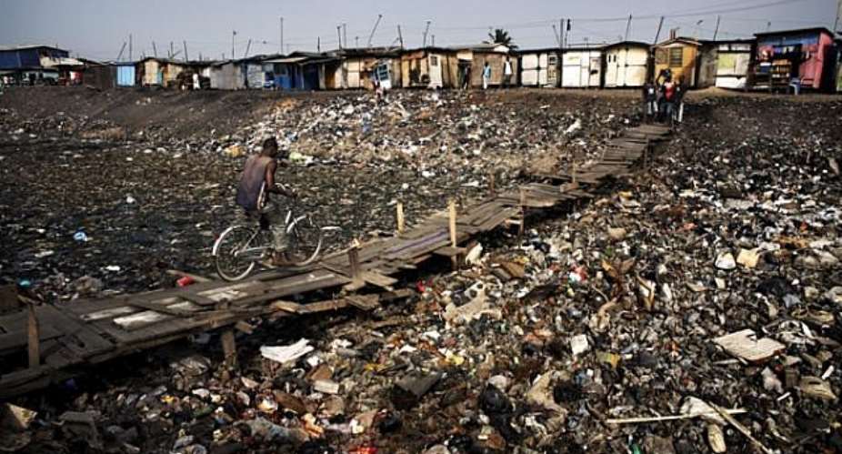 At the edge of the Agbogbloshie dump, a man cycles across a stretch of what was once part of the Korle Lagoon