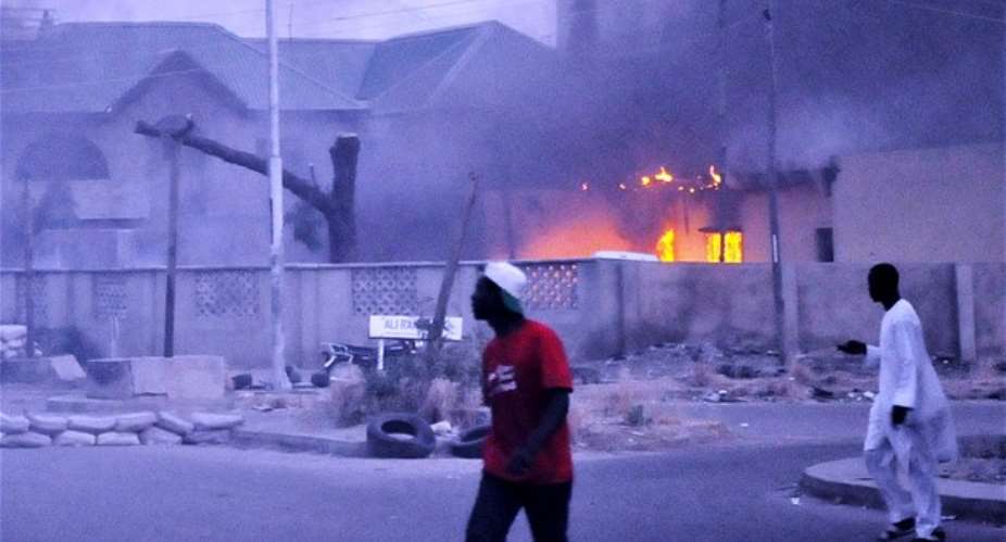 Residents pass by a burning police headquarters in Kano