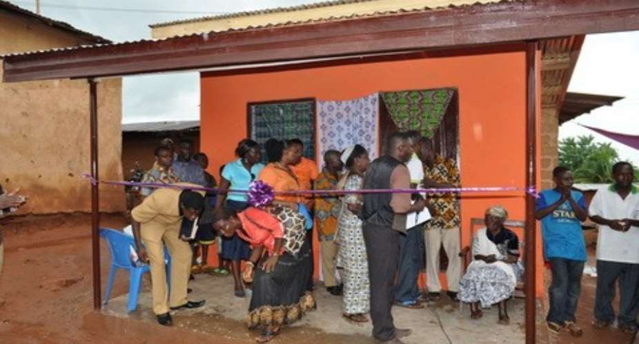 Maame Amanor sitting in front of her new house and surrounded by officials of Lesedi foundation as well as some well wishers.