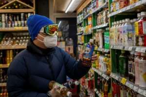 A man wearing a mask, goggles and gloves buys beverages at a supermarket in Beijing. By NICOLAS ASFOURI (AFP)