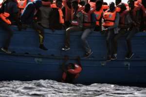 A migrant hangs from a boat as they wait to be rescued in the Mediterranean Sea off the coast of Libya on October 3, 2016